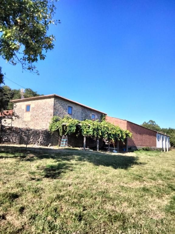 Casa de piedra con porche cubierto de hiedra en una colina cubierta de hierba bajo un cielo azul claro.