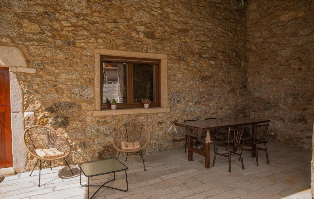 Patio de piedra con mesa y sillas de madera junto a un muro de piedra rústica y una ventana.