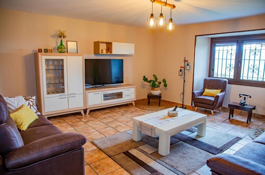 Acogedora sala de estar con sofá de cuero, mueble para la televisión, mesa de centro, sillas y una ventana junto a la pared.