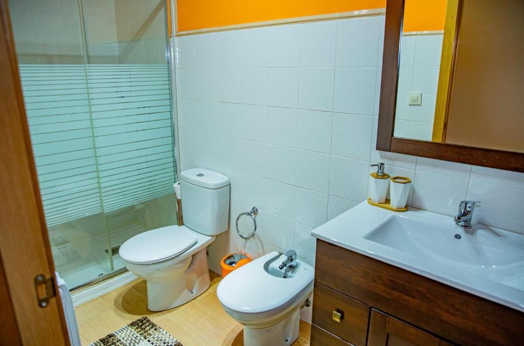 Baño pequeño con inodoro, bidé, lavabo, tocador de madera y puerta de ducha de vidrio esmerilado.