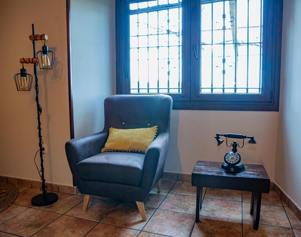 Acogedora sala de estar con sillón azul, mesita auxiliar con teléfono antiguo y luz de ventana.