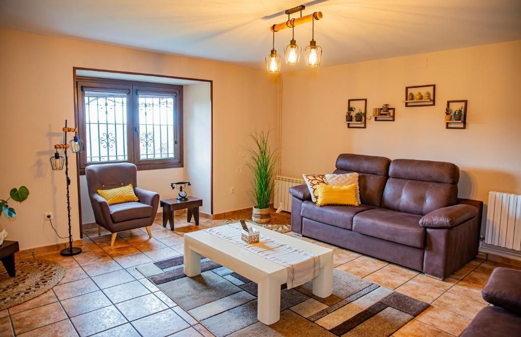 Acogedora sala de estar con sofá marrón, sillón, mesa de centro, ventana y cálidas lámparas colgantes.