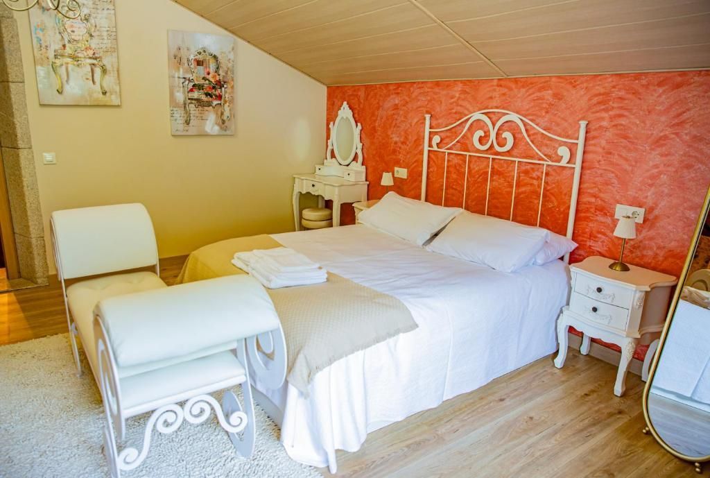 Habitación luminosa con pared decorativa de color coral, cama blanca, tocador, silla y decoración floral.