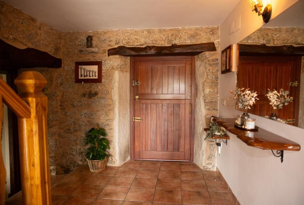 Pasillo rústico con puerta de entrada de madera, suelo de baldosas, paredes de piedra y una pequeña planta en maceta.
