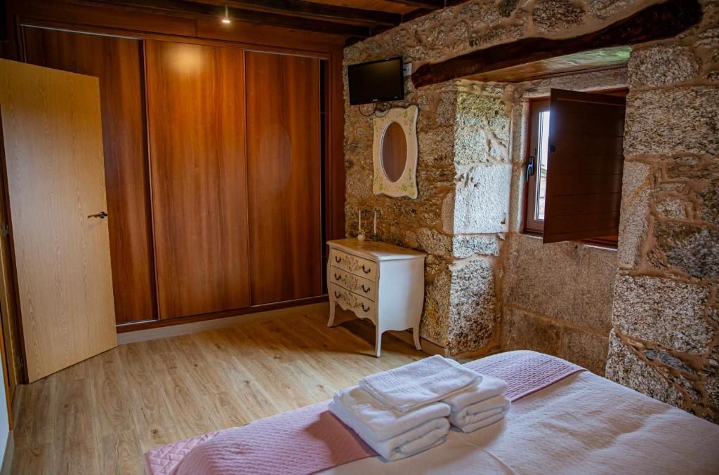 Habitación rústica con paredes de piedra, armario de madera, cama y toallas dobladas cerca de una ventana.