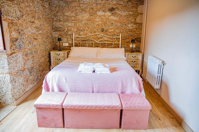 Cama rosa en un dormitorio rústico con pared de ladrillo visto y mesitas de noche pequeñas.