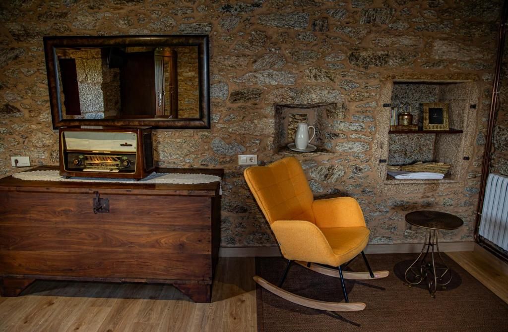 Habitación rústica con armario de madera, silla amarilla, pared de piedra y mesa redonda pequeña.