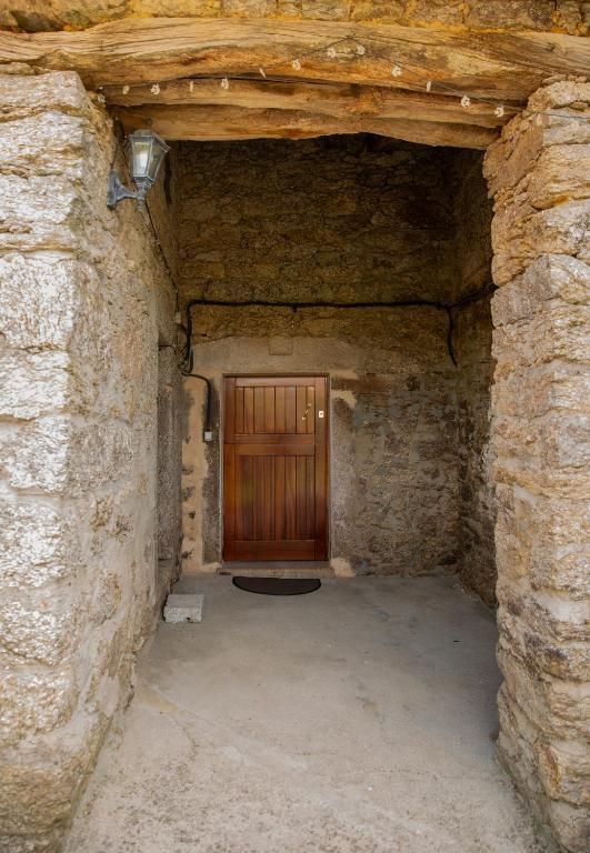 Entrada de piedra que da a una pequeña habitación con aspecto de cueva, con puerta de madera y suelo de tierra.
