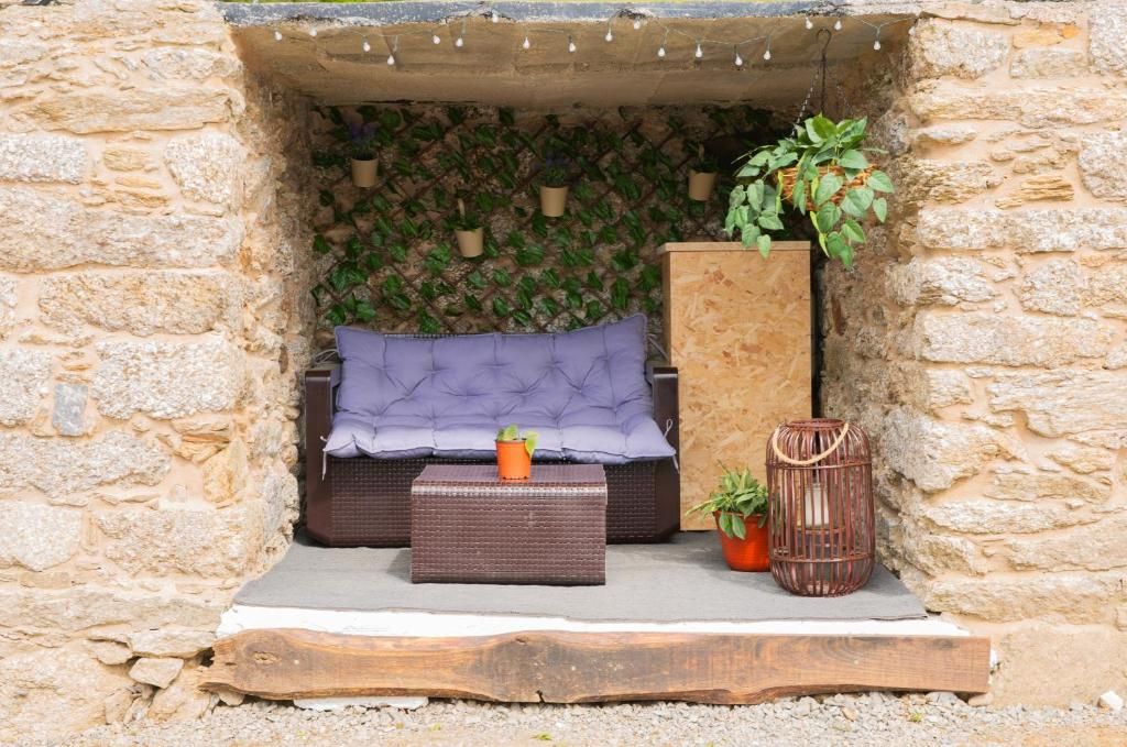 Asientos en un nicho de piedra con cojines morados, una mesita, plantas en macetas y una linterna de mimbre al aire libre.