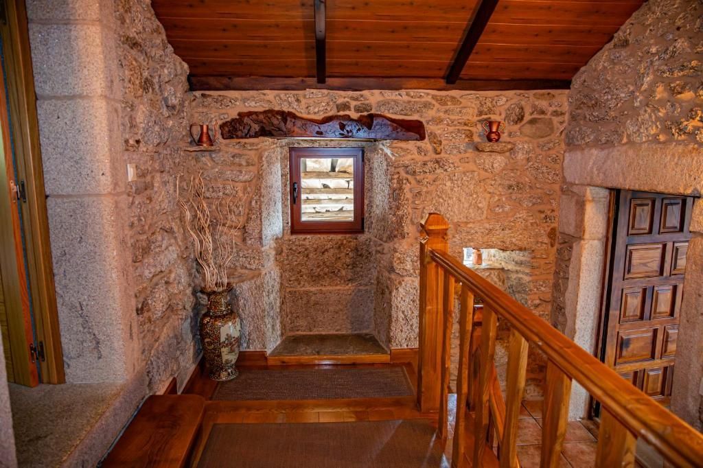 Pasillo interior de piedra con barandilla de madera, vigas a la vista y una pequeña ventana al final.