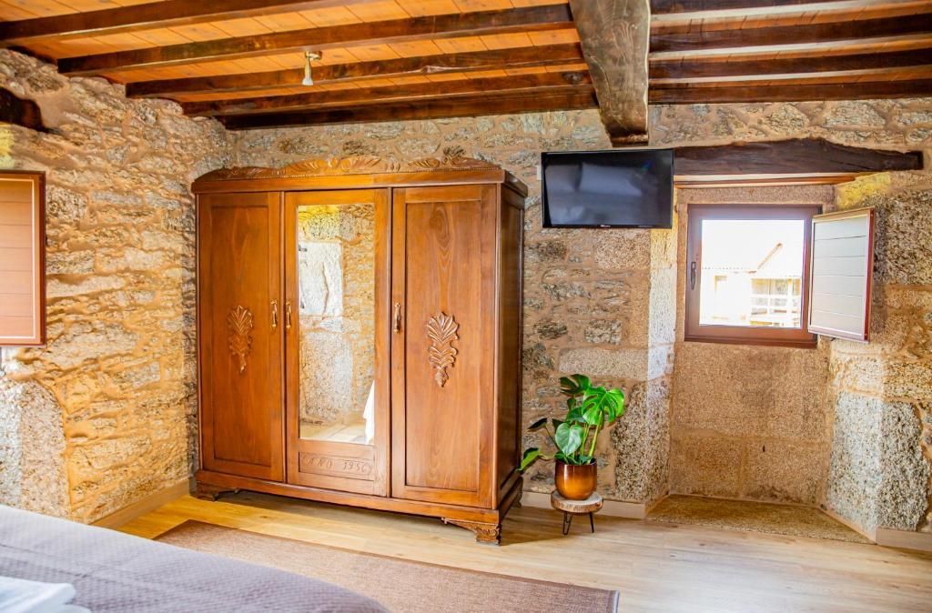 Habitación rústica de piedra con armario de madera, ventana, vigas vistas y planta en maceta.