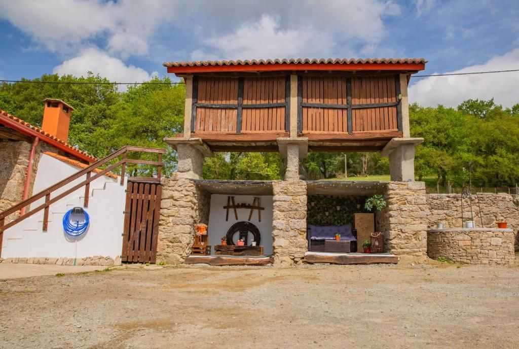 Puerta rústica de piedra con balcón superior de madera, enmarcada por árboles bajo un cielo nublado.