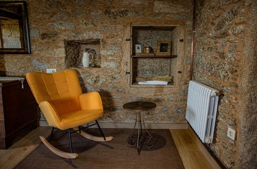Acogedora habitación rústica con un sillón naranja, una mesita, un nicho en la pared, un radiador y paredes de piedra.