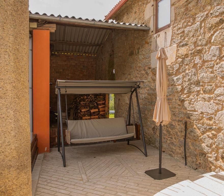 Patio de piedra con un banco columpio negro, sombrilla cerrada y pared naranja junto a un patio rústico.