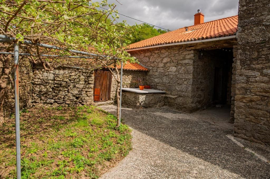Patio de piedra con tejados de tejas naranjas, una puerta de madera y un árbol que da sombra.
