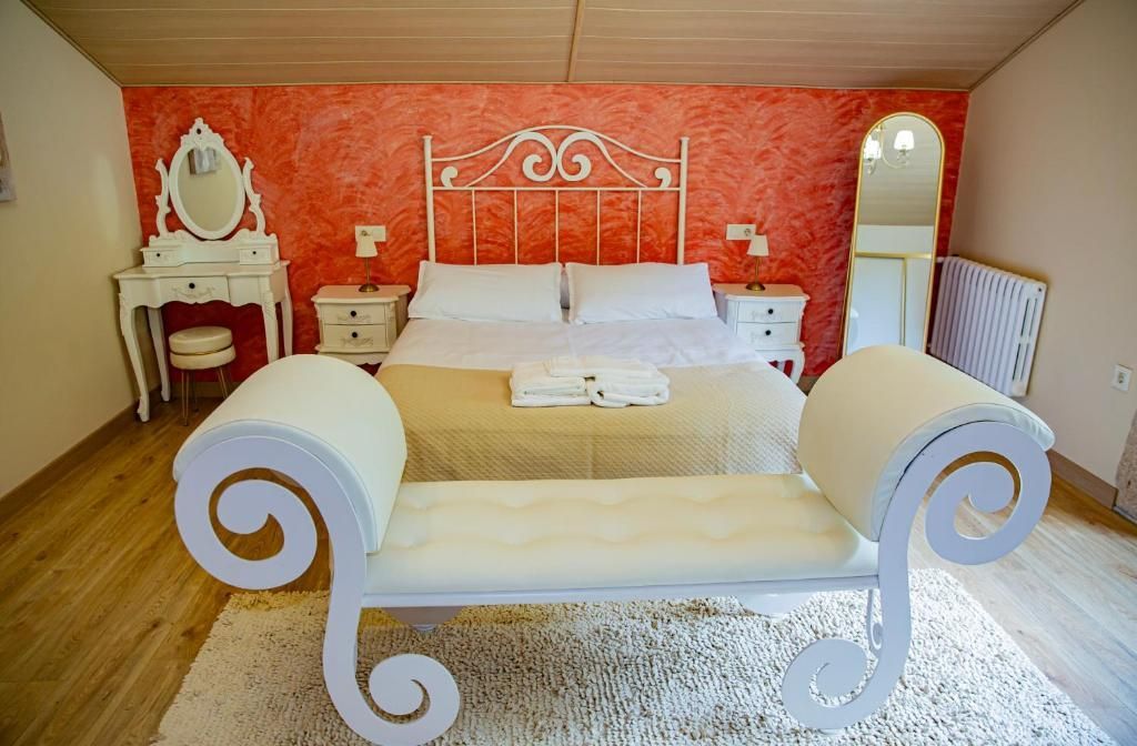 Elegante dormitorio con pared decorativa roja, cama blanca, tocador ornamentado y chaise longue blanca a juego.