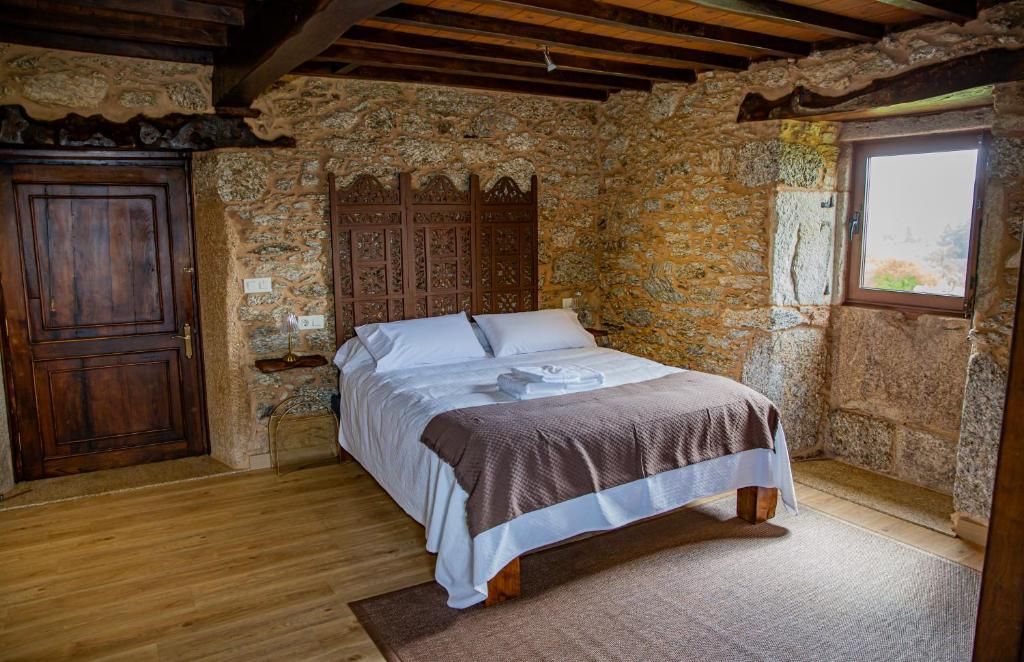 Habitación rústica con cama de madera, paredes de piedra, vigas vistas y una pequeña ventana.