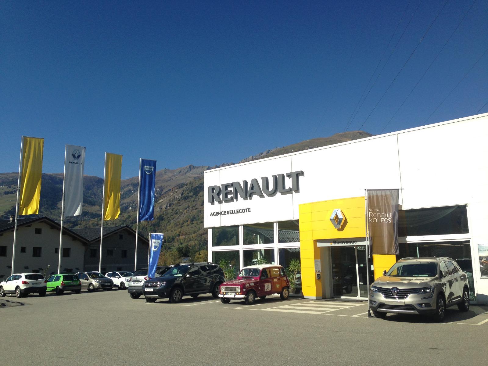 Concessionnaire Renault avec voitures garées à l'extérieur, montagnes en arrière-plan, journée ensoleillée.