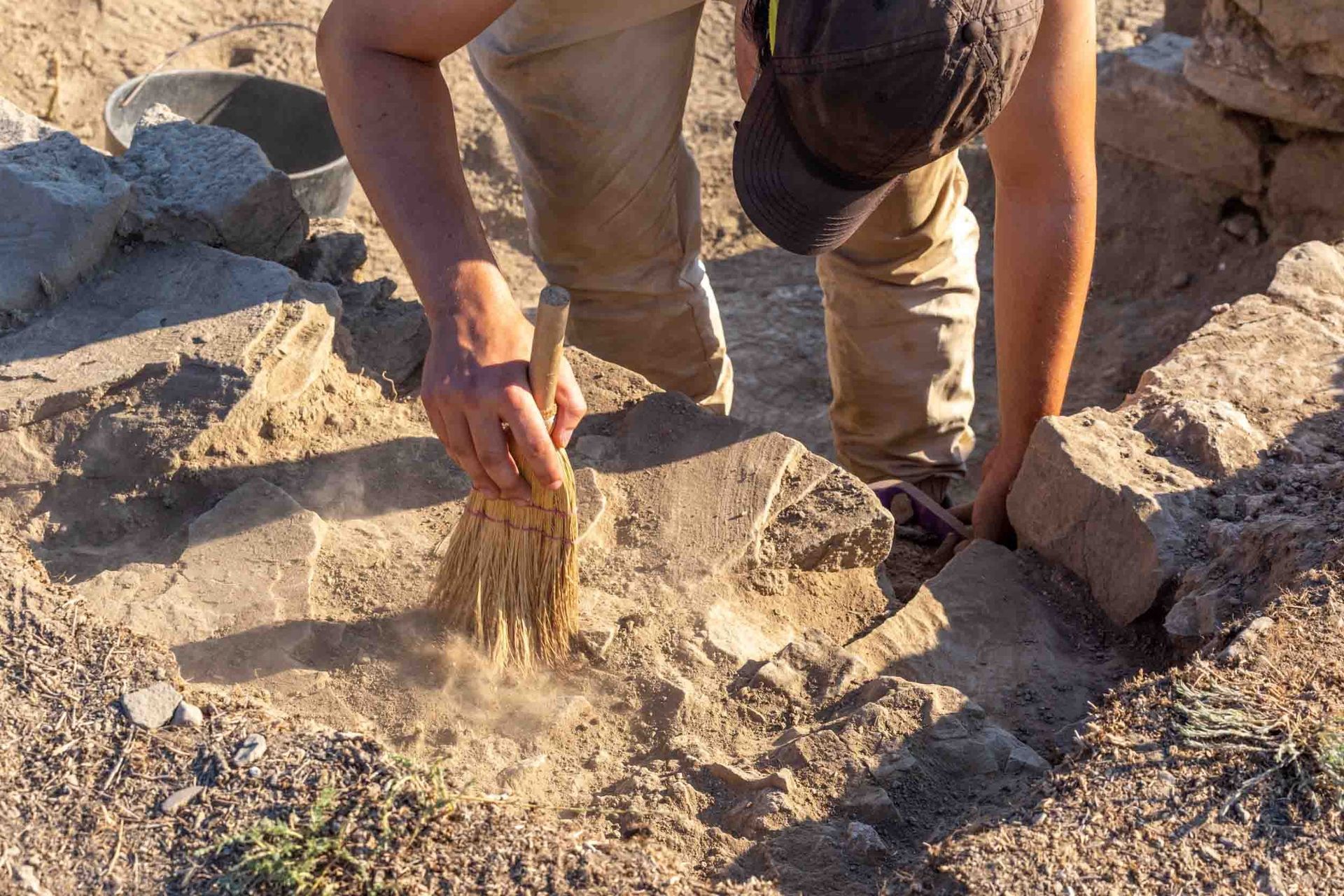 Un hombre está arrodillado en la tierra con un cepillo.
