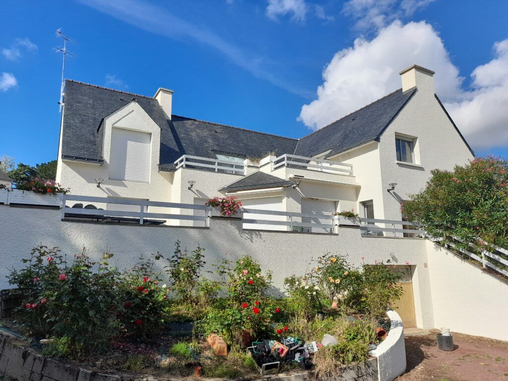 Une grande maison blanche avec un toit noir et un balcon
