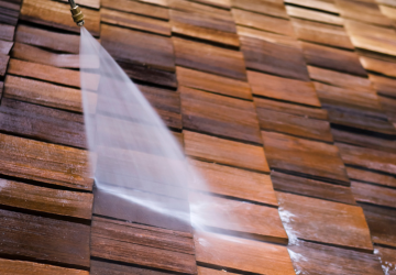 Une personne nettoie un toit en bois avec un nettoyeur haute pression.