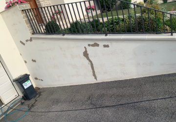 Un mur blanc avec une clôture noire et une poubelle devant.