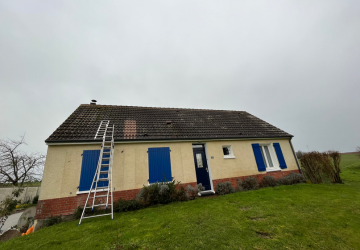 Une maison jaune avec des volets bleus et une échelle sur le toit.