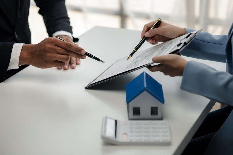 Ein Mann und eine Frau sitzen an einem Tisch und betrachten ein Klemmbrett und ein Modellhaus.