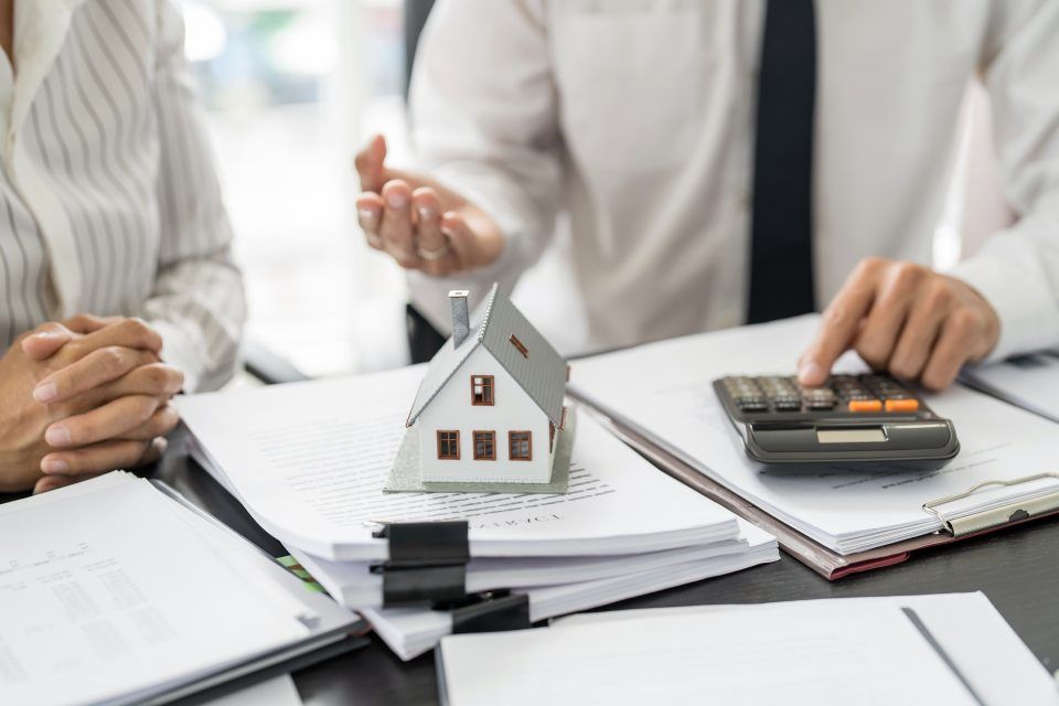 Ein Mann und eine Frau sitzen an einem Tisch mit einem Modellhaus und einem Taschenrechner.