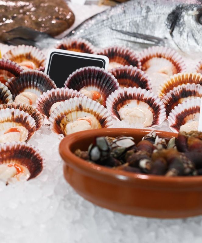 Un tazón de mejillones reposa sobre hielo junto a un tazón de vieiras.