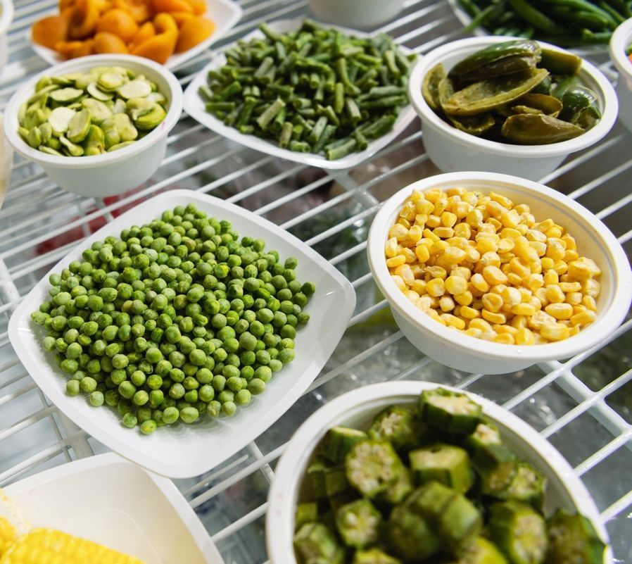Una variedad de verduras en un estante, incluidos guisantes, maíz y okra.