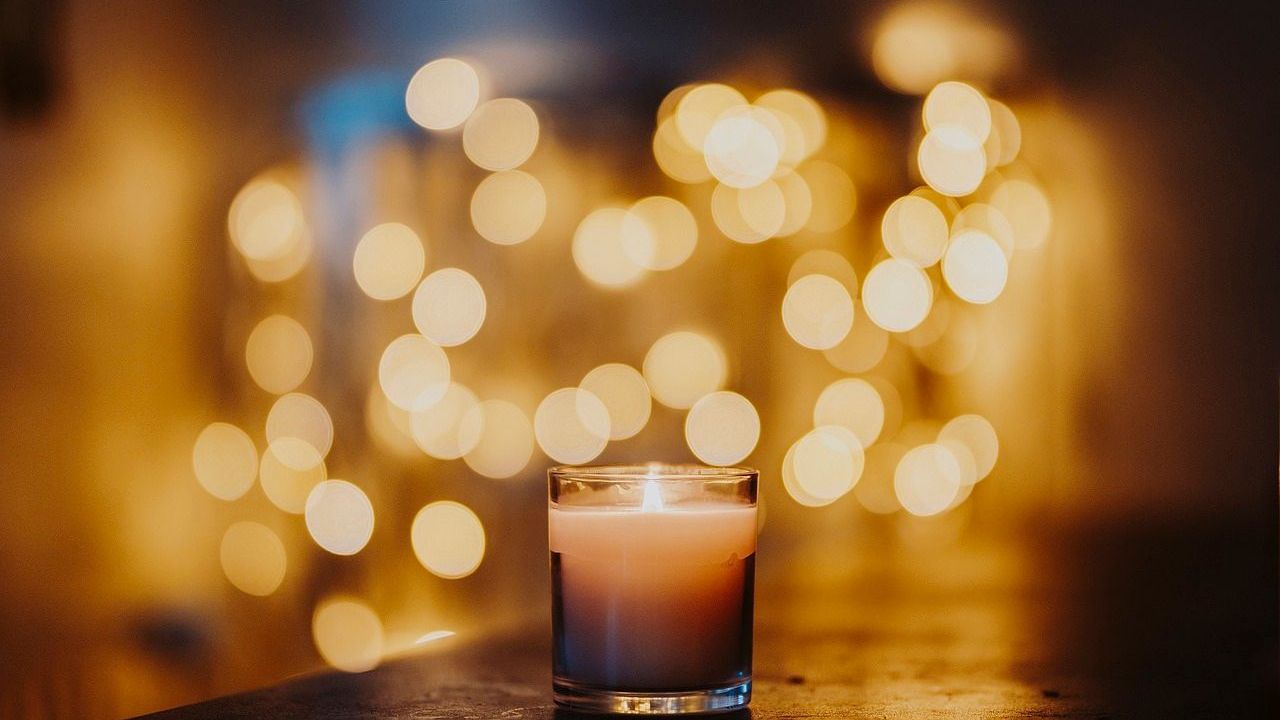 Eine Kerze in einem Glas mit warmem Licht, unscharfem Bokeh-Hintergrund.