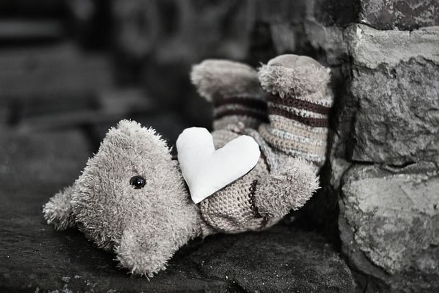 Grauer Plüschbär mit weißem Herz auf der Brust, liegend auf einer Steinoberfläche, Symbol für Kinder