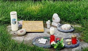 Gedenkstätte mit Steinen, Kerzen und Plakette auf grüner Wiese, Symbol für Trauer und Erinnerung.