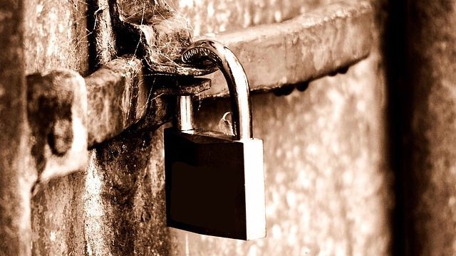 Rostiges Vorhängeschloss, das an einer Metallschließe geöffnet ist und an einer verwitterten Metalloberfläche befestigt ist.