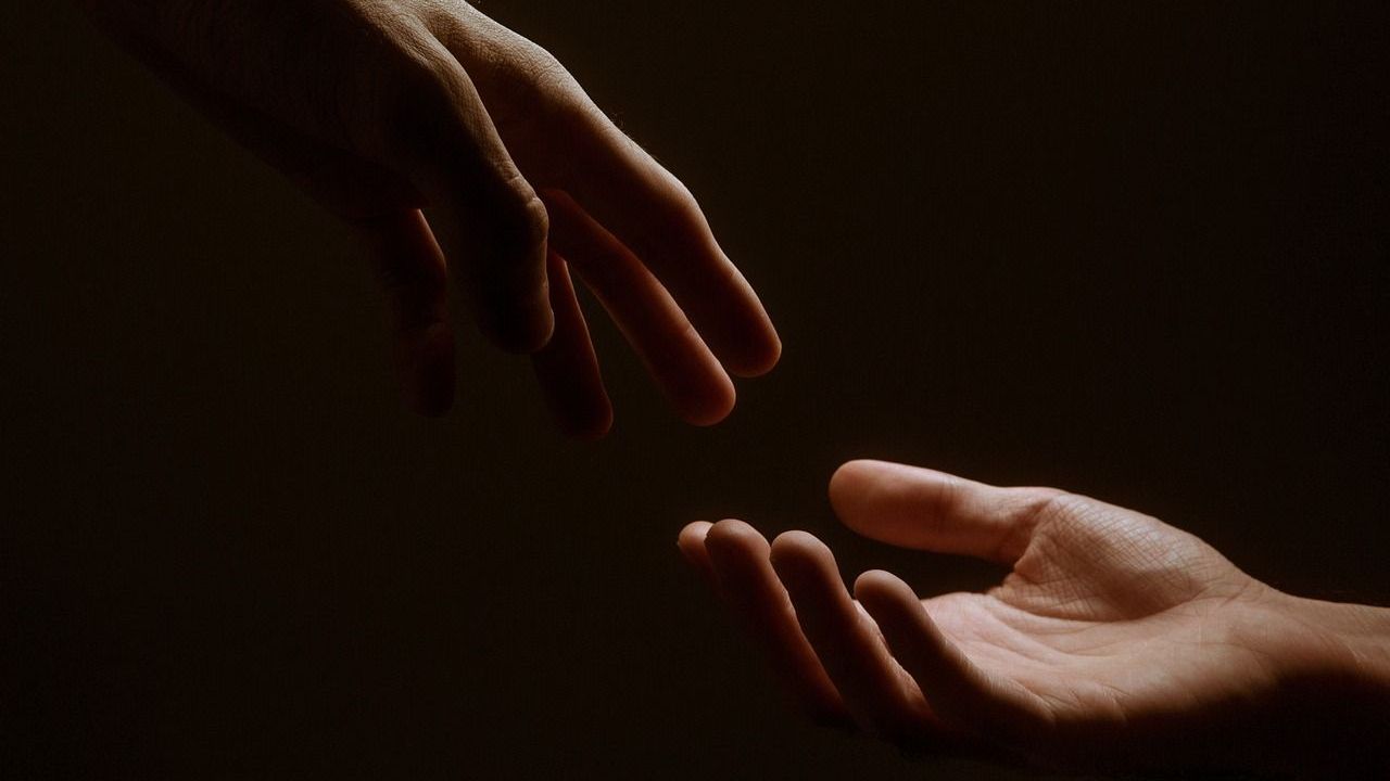 Two hands reaching towards each other, bathed in light against a dark background.