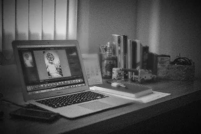 Laptop auf Schreibtisch, auf dessen Bildschirm ein Porträt zu sehen ist; daneben liegen Bücher