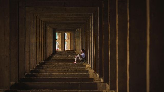 Person, die auf den Stufen eines langen, dunklen Tunnels sitzt und zum Licht am Ende blickt.