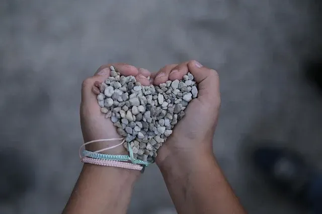 Zwei Hände, die eine Schale bilden, halten einen Haufen kleiner, grauer Kieselsteine ​​in Herzform.