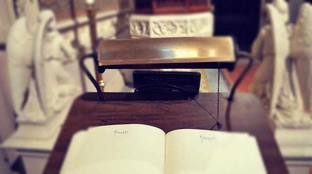 Open book on wooden stand with lamp above.  Statues are in the blurred background.