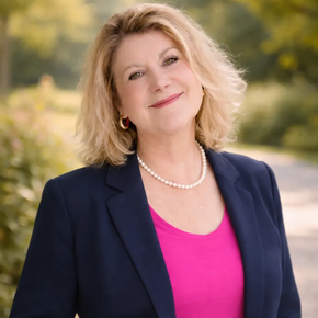 Patricia Rind TrostWorte freie Trauerreden und Trauerbegleitung Ein professionelles Porträtfoto einer lächelnden Person in einem marineblauen Blazer, einem rosa Oberteil und einer Perlenkette vor einer verschwommenen Gartenkulisse.