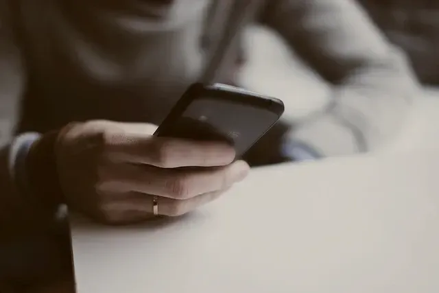 Hände, die ein Smartphone über einem weißen Tisch in einem sanft beleuchteten Innenraum halten