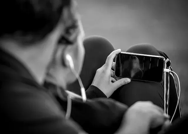 KI-Avatare versprechen Trost, doch die Forschung warnt: Sie stören den Trauerprozess, fördern Abhängigkeit und verfälschen echte Erinnerungen. Eine Einordnung. Eine Person, die ein Smartphone im Querformat in der Hand hält und Kopfhörer trägt