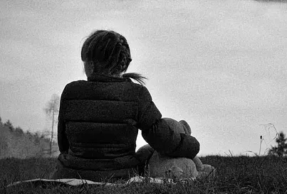 Wenn Kinder trauern, brauchen sie Schutz und echte Begleitung. Warum KI-Avatare für trauernde Kinder besonders gefährlich sind und was die Forschung warnt. Ein Kind in einer Daunenjacke sitzt im Gras und blickt in der Abenddämmerung über eine ruhige Landschaft