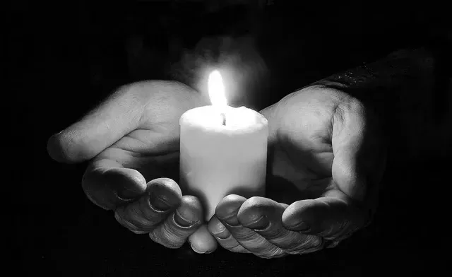 Echte Trauerbegleitung bedeutet Anwesenheit, Ehrlichkeit und menschliche Wärme. Was KI nicht leisten kann und warum das in der Trauer alles entscheidet. Hände, die eine brennende weiße Kerze umschließen, in Schwarz-Weiß.