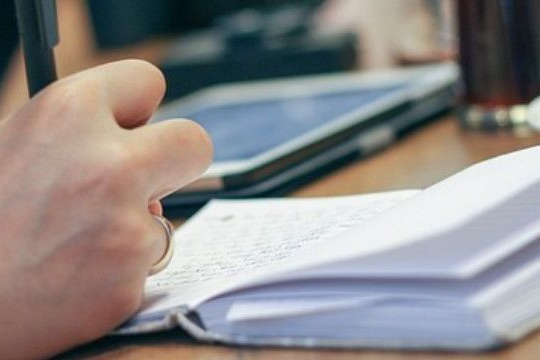 Vorsorge, Trauerredenvorsorge, Fürsorge für den Todesfall Eine Hand die in ein offenes Notizbuch schreibt, ein Tablet im Hintergrund