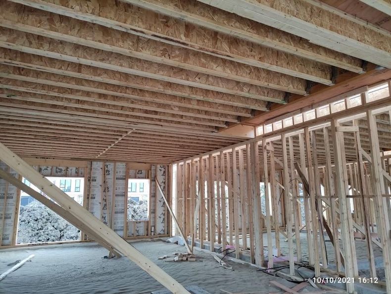 Intérieur d'une maison en bois brut, avec poutres de plafond apparentes, montants muraux et contreventements diagonaux.