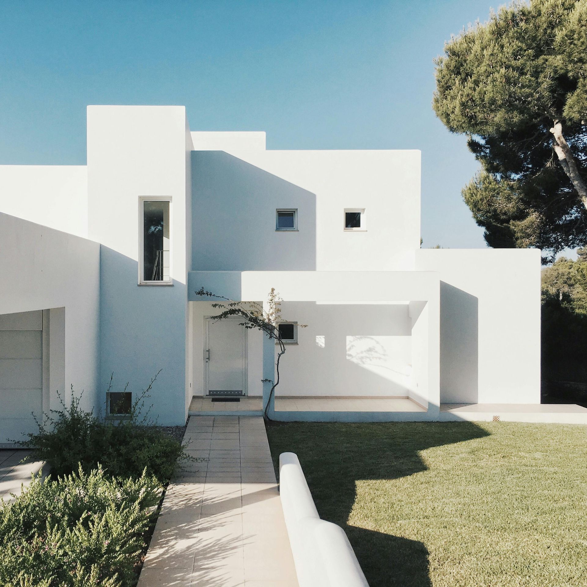 Maison blanche moderne avec toit plat, allée d'entrée et pelouse verte sous un ciel dégagé