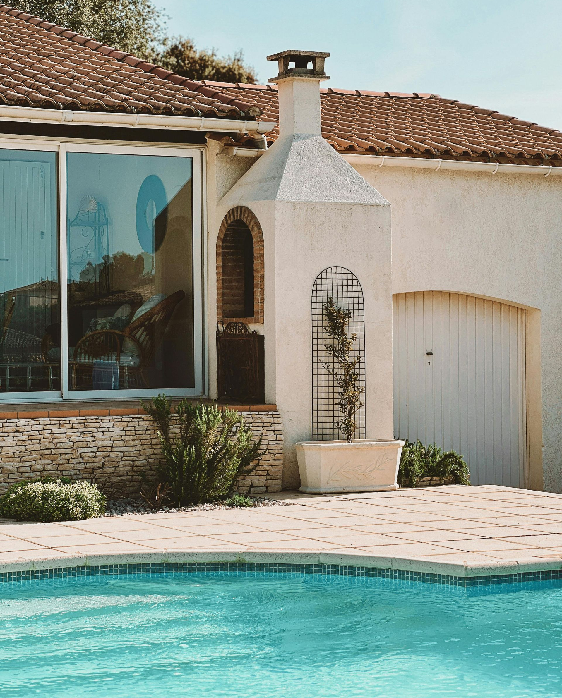 Villa en stuc au bord de la piscine, avec toit en tuiles de terre cuite, niche cintrée et portes coulissantes.