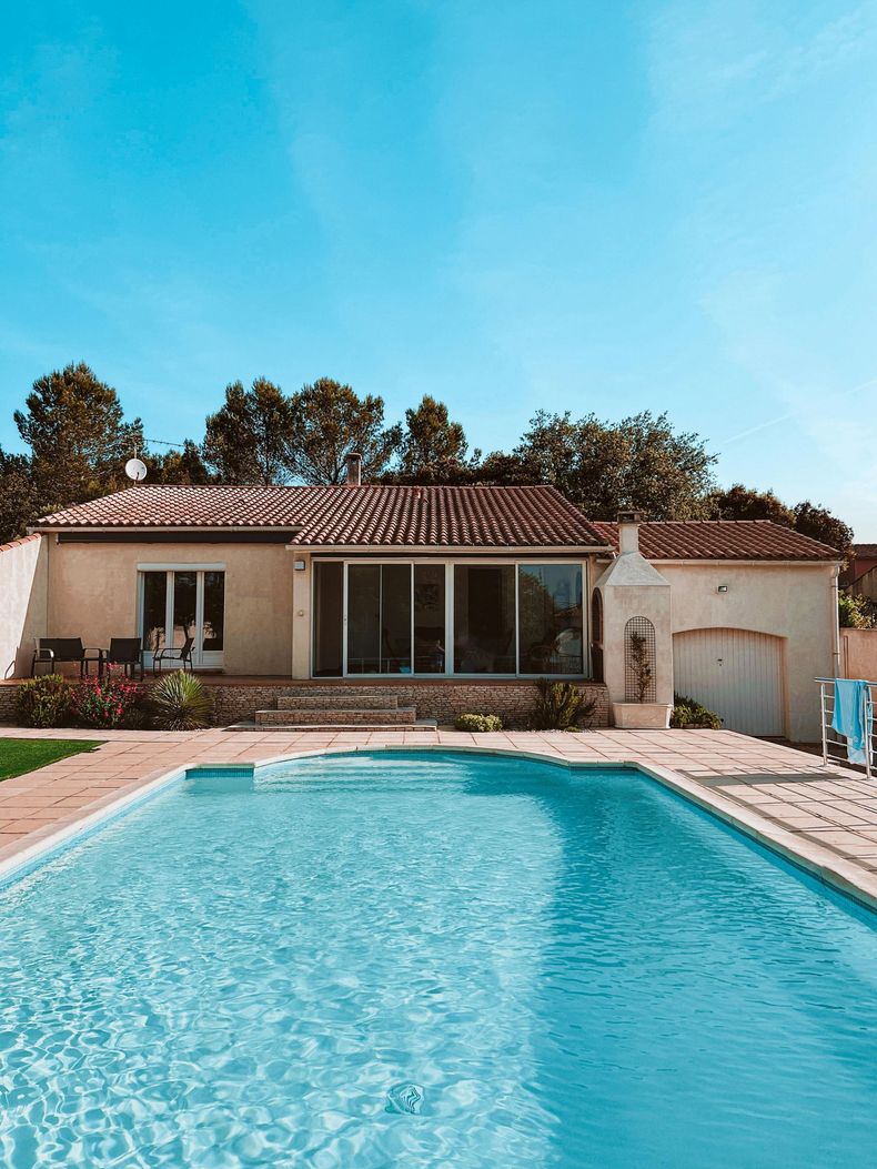 Maison avec jardin, piscine turquoise, terrasse et ciel bleu